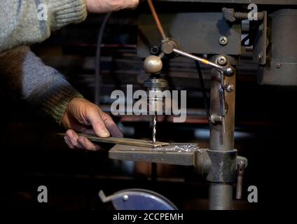 Blacksmith uses drill press in garage. A close up view of a metalworker operating a bench drill inside his workshop. Heavy duty machine is used for dr Stock Photo