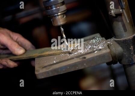 Blacksmith uses drill press in garage. A close up view of a metalworker operating a bench drill inside his workshop. Heavy duty machine is used for dr Stock Photo