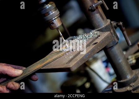 Blacksmith uses drill press in garage. A close up view of a metalworker operating a bench drill inside his workshop. Heavy duty machine is used for dr Stock Photo