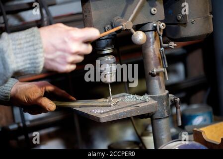 Blacksmith uses drill press in garage. A close up view of a metalworker operating a bench drill inside his workshop. Heavy duty machine is used for dr Stock Photo