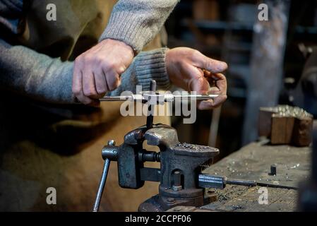 Professional blacksmith working with metal  at forge, workshop. Handmade, craftsmanship and blacksmithing concept Stock Photo