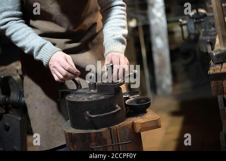 Professional blacksmith working with metal  at forge, workshop. Handmade, craftsmanship and blacksmithing concept Stock Photo