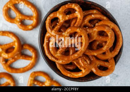 Mini pretzels with salt in a ceramic bowl close-up. Traditional German beer appetizer on a grey background. Selective focus, top view Stock Photo