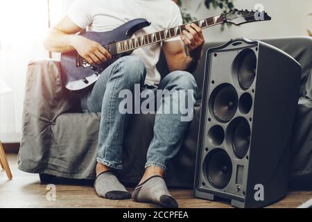 Unrecognizable man sitting on the sofa in his room and playing electric guitar Stock Photo