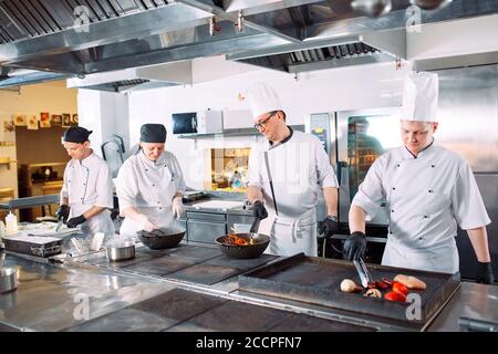 Five chefs wearing uniforms posing in a kitchen . Stock Photo