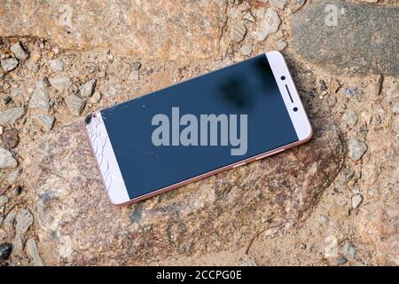 pink new phone with broken screen lies on rocks Stock Photo