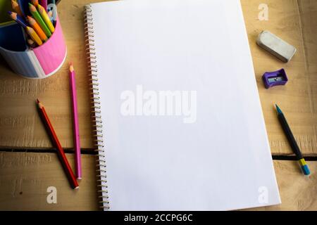 top view of an empty white notebook space for text, color pencils, eraser, sharpener and pencil on wooden table Stock Photo
