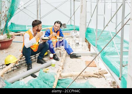 Positive engineer and contractor having lunch at construction site, eating noodles and discussing news and work Stock Photo