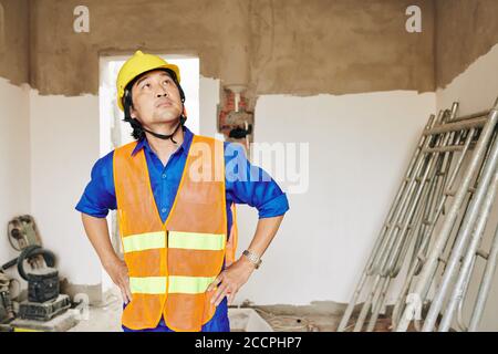 Pensive unhappy builder looking at water stains on ceiling and planning repairing of leaking roof Stock Photo