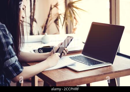 Student work process concept. Young Asisn woman working university project with generic design laptop. Analysis plans hands, using smartphone. Stock Photo