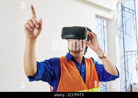 Serious builder in brigh orange vest and headset testing augmented reality application Stock Photo
