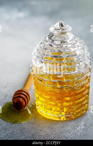 Liquid flower honey in a glass jar with wooden honey dipper on a concrete or stone background. Selective focus, copy space Stock Photo