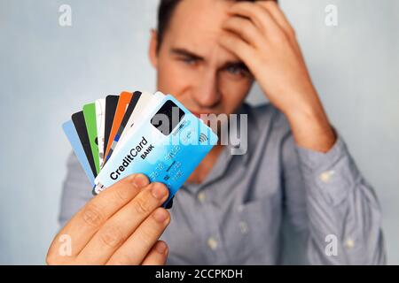 Thoughtful mixed race businessman looking at credit cards. Pensive handsome young male manager thinking of his profit and choosing credit card. Many Stock Photo