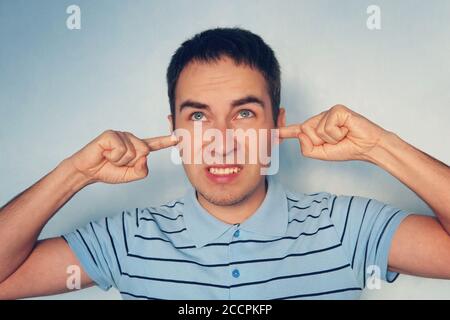 Closeup portrait young, angry, unhappy, stressed man covering his ears, looking up, to say, stop making loud noise it's giving headache, blue Stock Photo