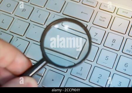 Male hand holds the magnifying glass above the laptop english layout with blank enter key. Your word on a empty computer keypad button. Designer Stock Photo