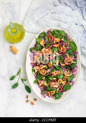Healthy vegetarian salad of red cabbage, fresh organic spinach, pickled onions with walnuts, olive oil and mustard dressing in a light plate on a marb Stock Photo