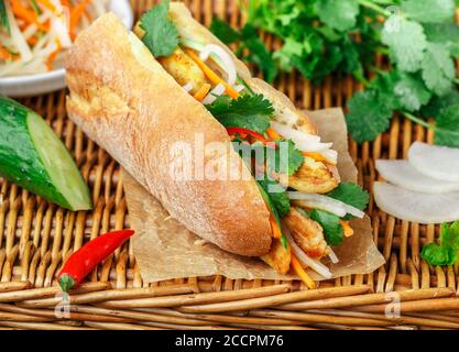 Baguette sandwich with fried chicken and fresh vegetables-carrots, cucumber, daikon, red pepper and cilantro (coriander) on a wicker table. Delicious Stock Photo