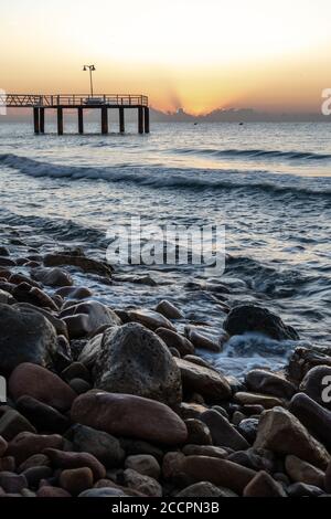 Sunrise from a pebble beach with a walkway to the sea Stock Photo