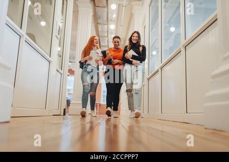 Smiling female students walking through university corridor after their class. Group of college students after lecture. Stock Photo