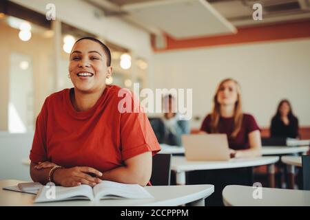 Female student sitting in university classroom and smiling. Woman paying attention in the class. Stock Photo