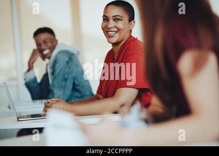 Smiling female student talking with classmates in classroom. Students chatting in high school classroom. Stock Photo