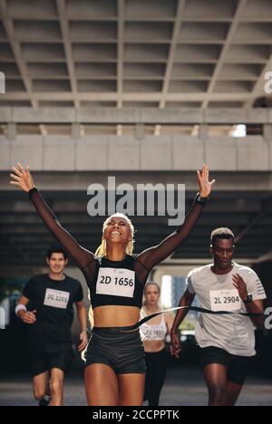 African woman finishing the run at the marathon competition. Female athlete crosses the finish line first and winning the marathon. Stock Photo