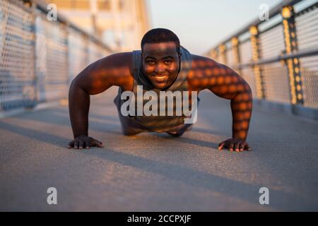 Young african-american man is exercising on the bridge in the city. He is doing push-ups. Stock Photo