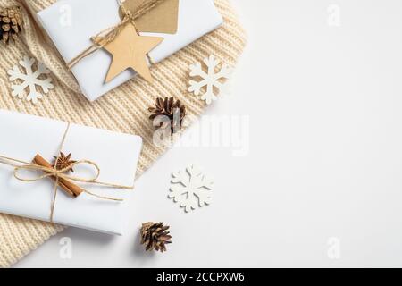 Handmade Christmas gift boxes, white wooden snowflakes and decorations, knitted plaid and pine cones on white background. Flat lay, top view. Vintage Stock Photo