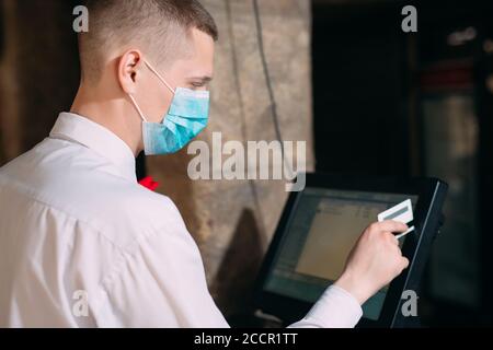 small business, people and service concept. man or waiter in medical mask at counter with cashbox working at bar or coffee shop. Stock Photo