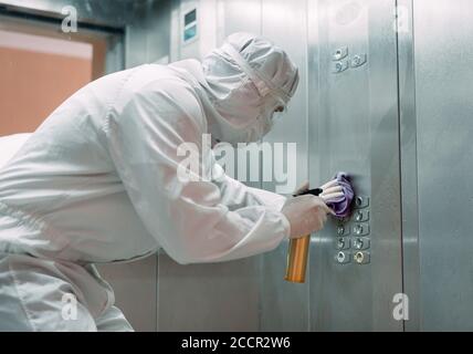 Coronavirus infection. Paramedic in protective mask and costume disinfecting an elevator with sprayer, Stock Photo