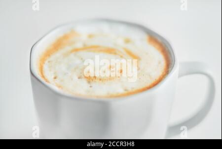 Light faceted cup with a delicate cappuccino with caramel and thick foam on a light background. An invigorating drink in the early morning. Stock Photo