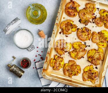Oven baked whole crushed and crusty potato with coarse sea salt, olive oil, garlic, pepper and thyme in metallic tray. Roasted smashed potatoes. Austr Stock Photo