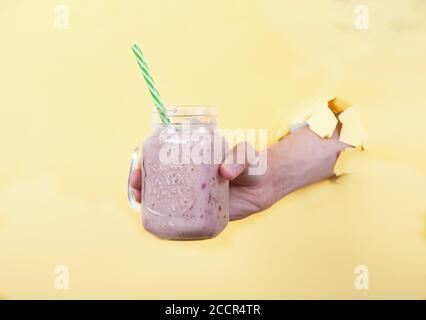 A man's hand holds a fresh smoothie made from milk and cherries in a glass jar on a yellow background. Copy spaes Stock Photo