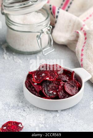 Healthy organic Purple Baked Beet (beetroot) Chips with olive oil and large Sea Salt in a white bowl on a grey concrete background. Dietary useful sna Stock Photo