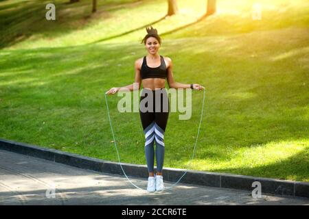 Joyful black girl training at park, using jumping rope Stock Photo