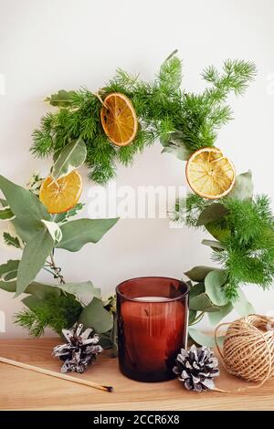Christmas home decor. Hand made wreath decorated with dry oranges, candle and pine cones on wooden table Stock Photo