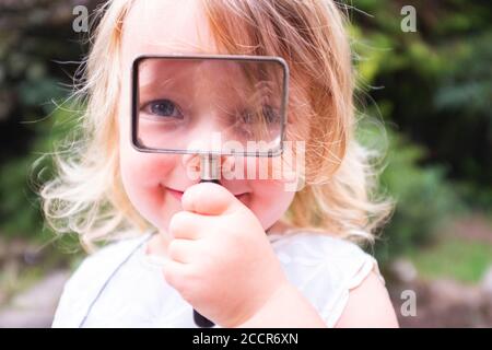 Young child female 3 years old playing outdoors in the woods with a magnifying glass looking for bugs and insects to look at Stock Photo