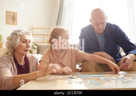 Portrait of cure red haired girl playing board games with grandparents while enjoying time together in cozy home lit by sunlight Stock Photo
