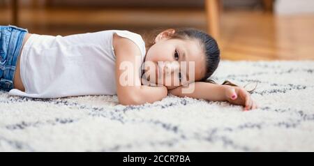 Bored Chinese Little Girl Lying On Floor At Home, Panorama Stock Photo
