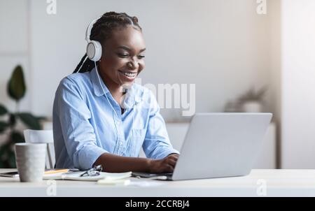 Black secretary working on laptop and listening music in headphones at office Stock Photo