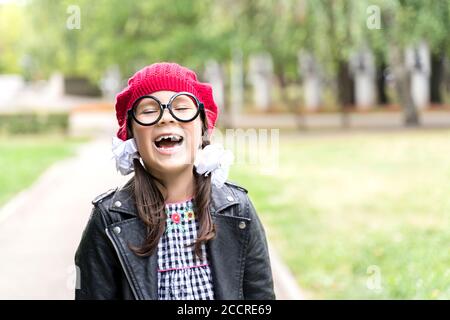 a funny little girl in a red cap and round glasses laughs Stock Photo