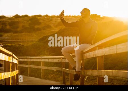 Latin man taking selfies with a smartphone over an amazing sunset landscape view. Natural  outdoor light Stock Photo