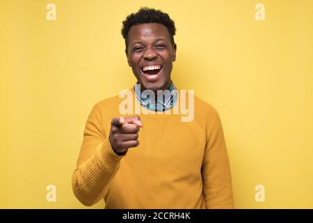 Handsome african man in yellow sweater pointing at camera on joke. Stock Photo