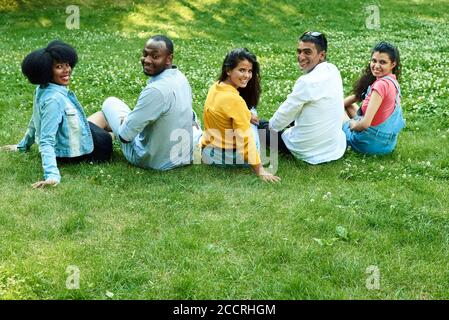 Five black people together are sitting on the grass. A company of friends is sitting on the grass in the park. Stock Photo