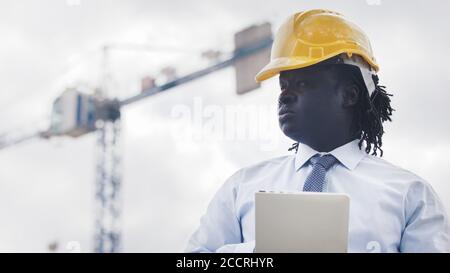 Portrait of an african man with hardhat using tablet on the construction site and observing the work. High quality photo Stock Photo
