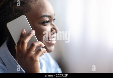 Mobile Communication. Closeup of smiling black woman talking on cellphone, side view Stock Photo