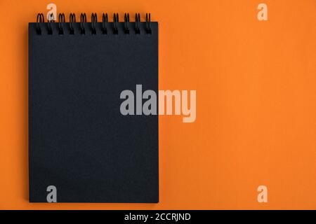 Black blank notepad on an orange background. Minimalistic halloween celebration design. Mock up. Top view, copy space. Flat lay. Stock Photo