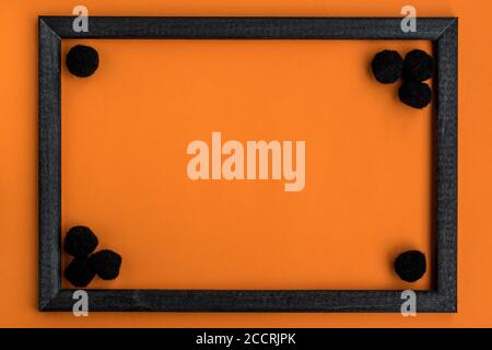 Halloween black wooden frame with black fluffy pom-poms with copy space for text on orange background. Flat lay, top view. Festive theme. Mock up. Stock Photo