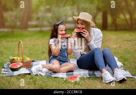 Mom And Daughter Enjoying Family Picnic Eating Watermelon In Park Stock Photo