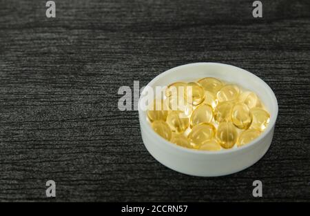 Yellow soft shell D-vitamin capsule in bowl. Fish oil capsules with omega 3 and vitamin D on dark wooden background, healthy diet concept. Pills and c Stock Photo